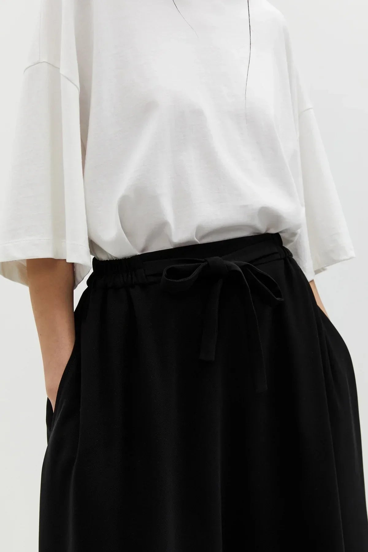 Close-up of a person wearing a white oversized t-shirt and black wide skirt with tie waist and pockets