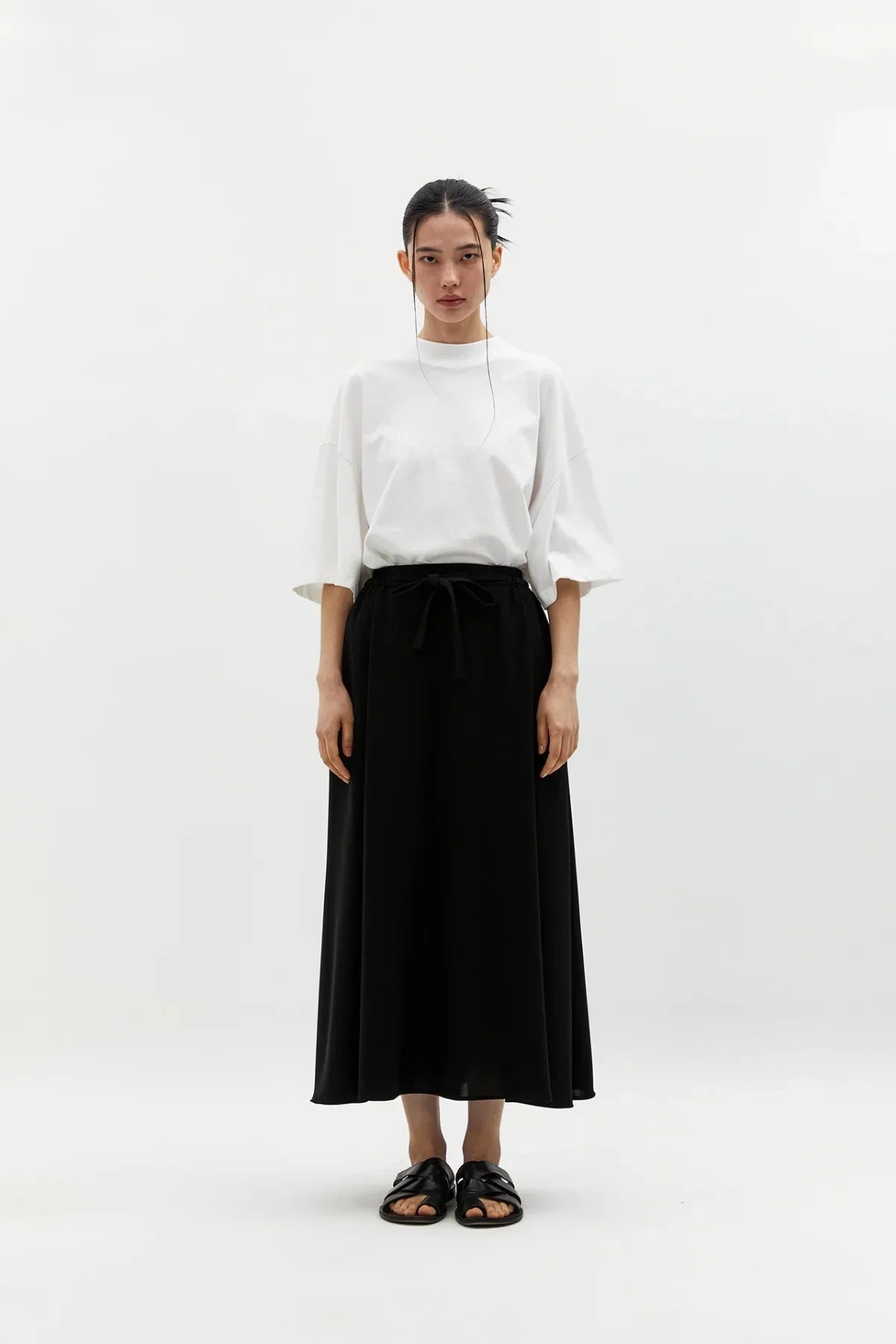 Model wearing wide black skirt with drawstring waist, white oversized t-shirt, and black sandals on white background