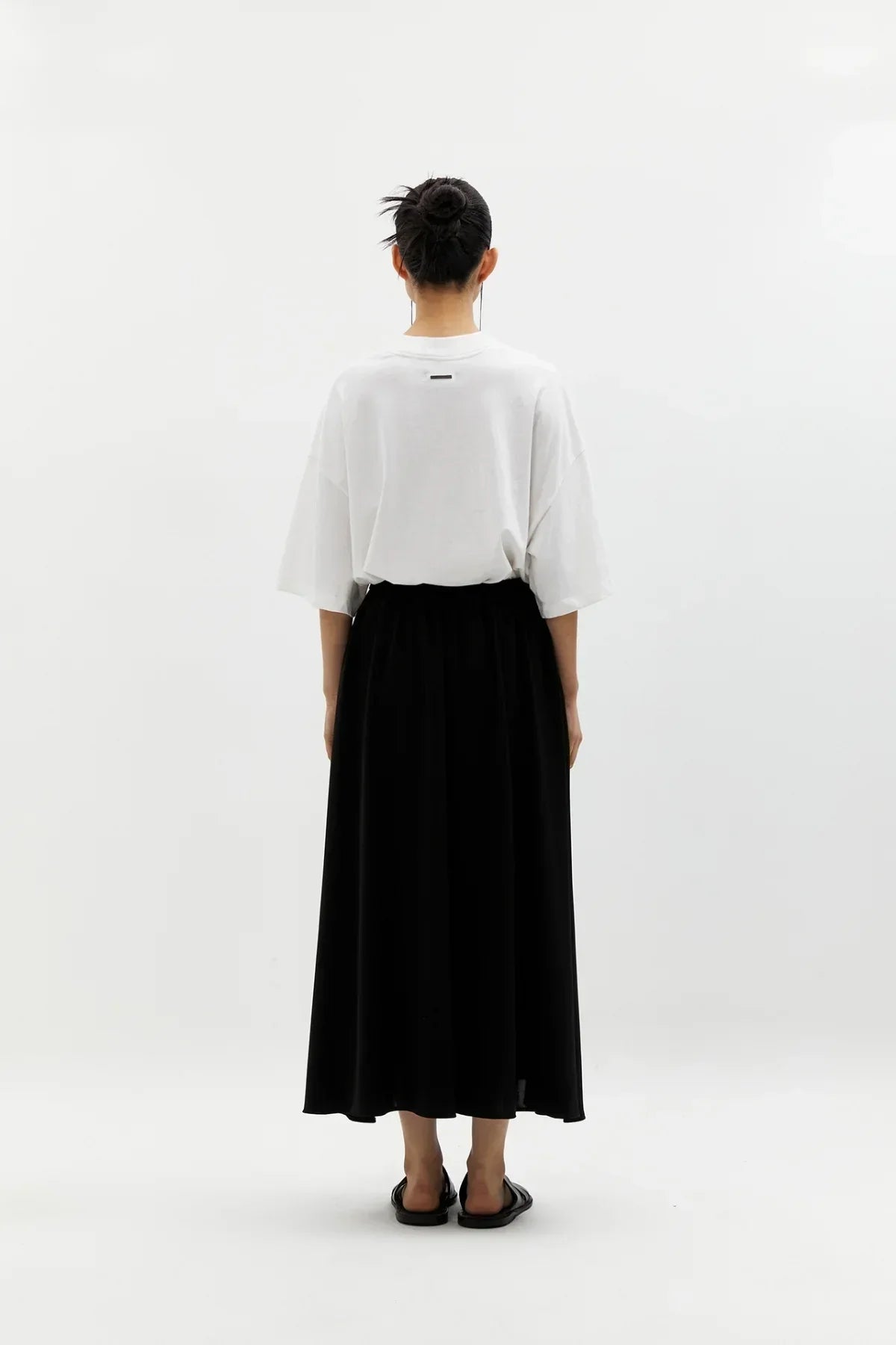 Rear view of woman wearing black wide skirt and white oversized t-shirt in studio