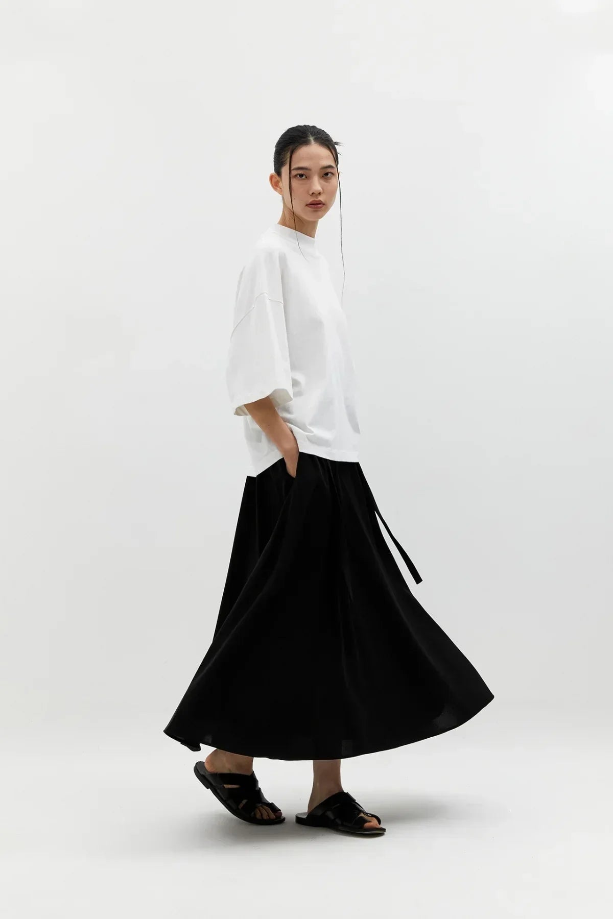 Woman modeling black wide skirt and white oversized t-shirt in minimalist studio