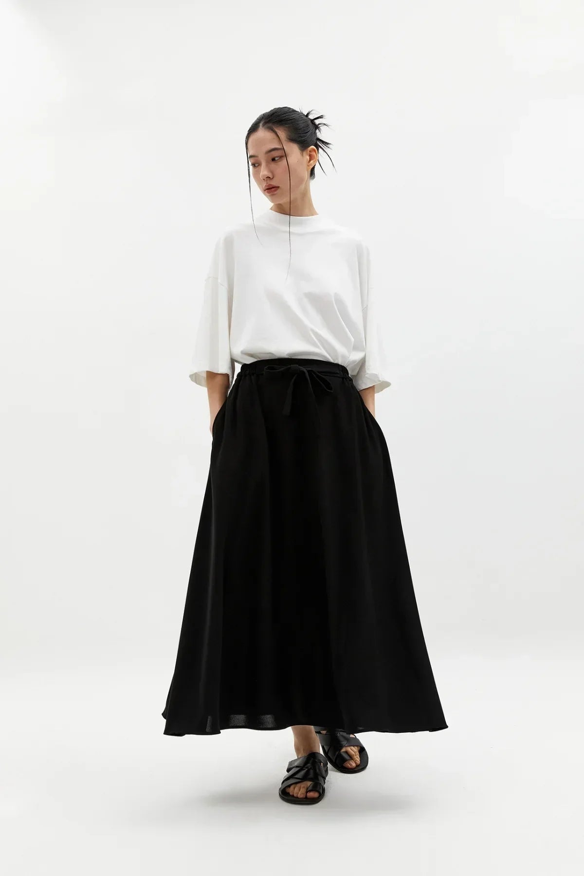 Woman wearing a white oversized T-shirt and a black wide skirt with sandals in a studio