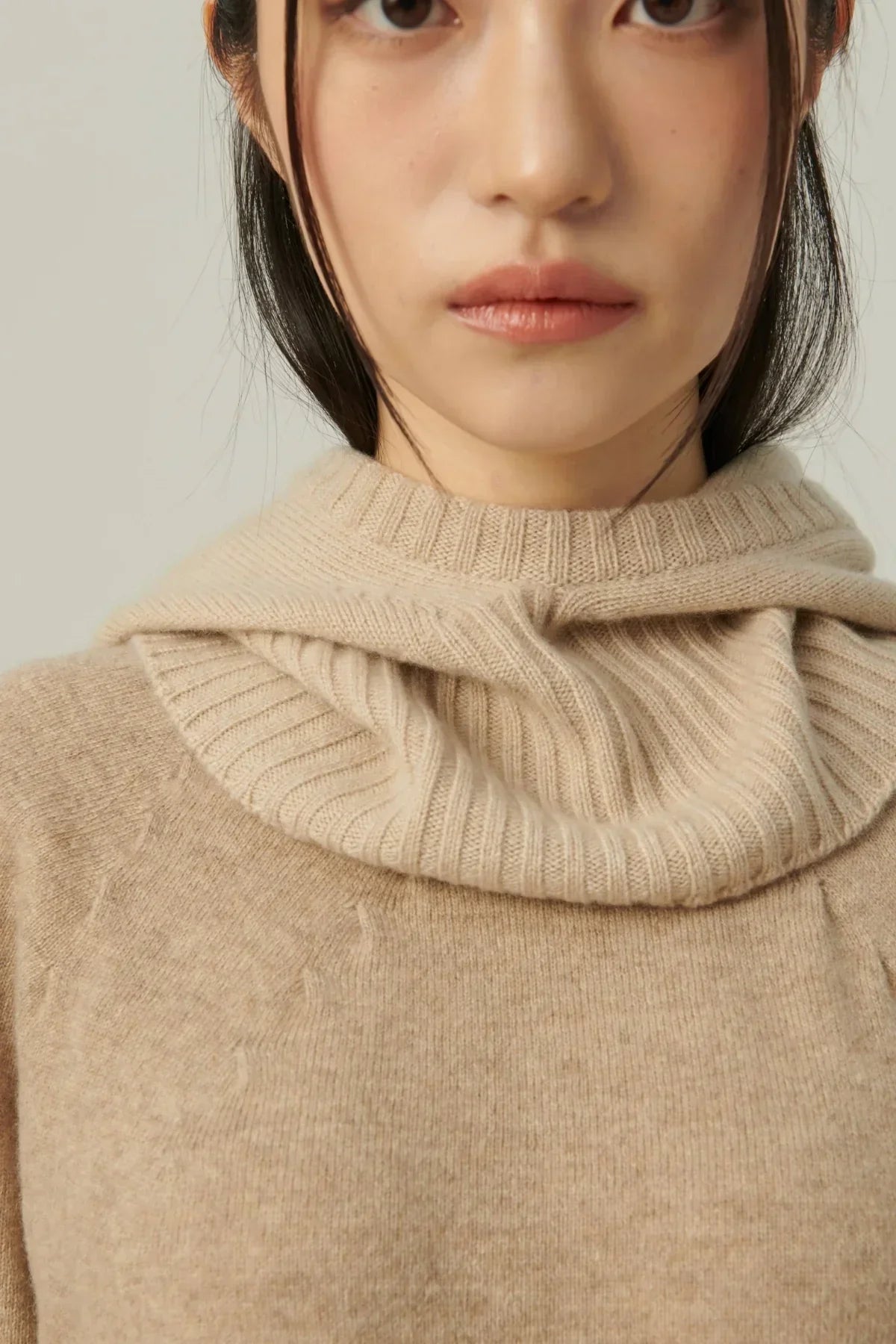 Close-up of woman wearing beige minimal cashmere balaclava and sweater with ribbed texture