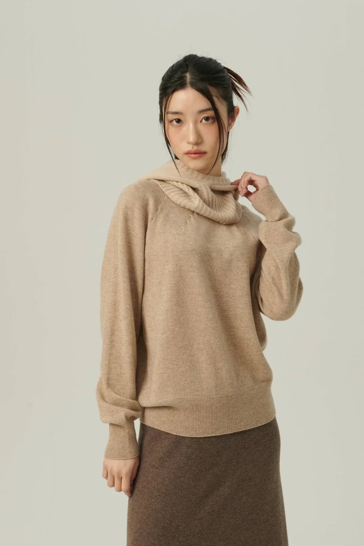 Young woman wearing beige cashmere sweater and brown skirt against neutral background