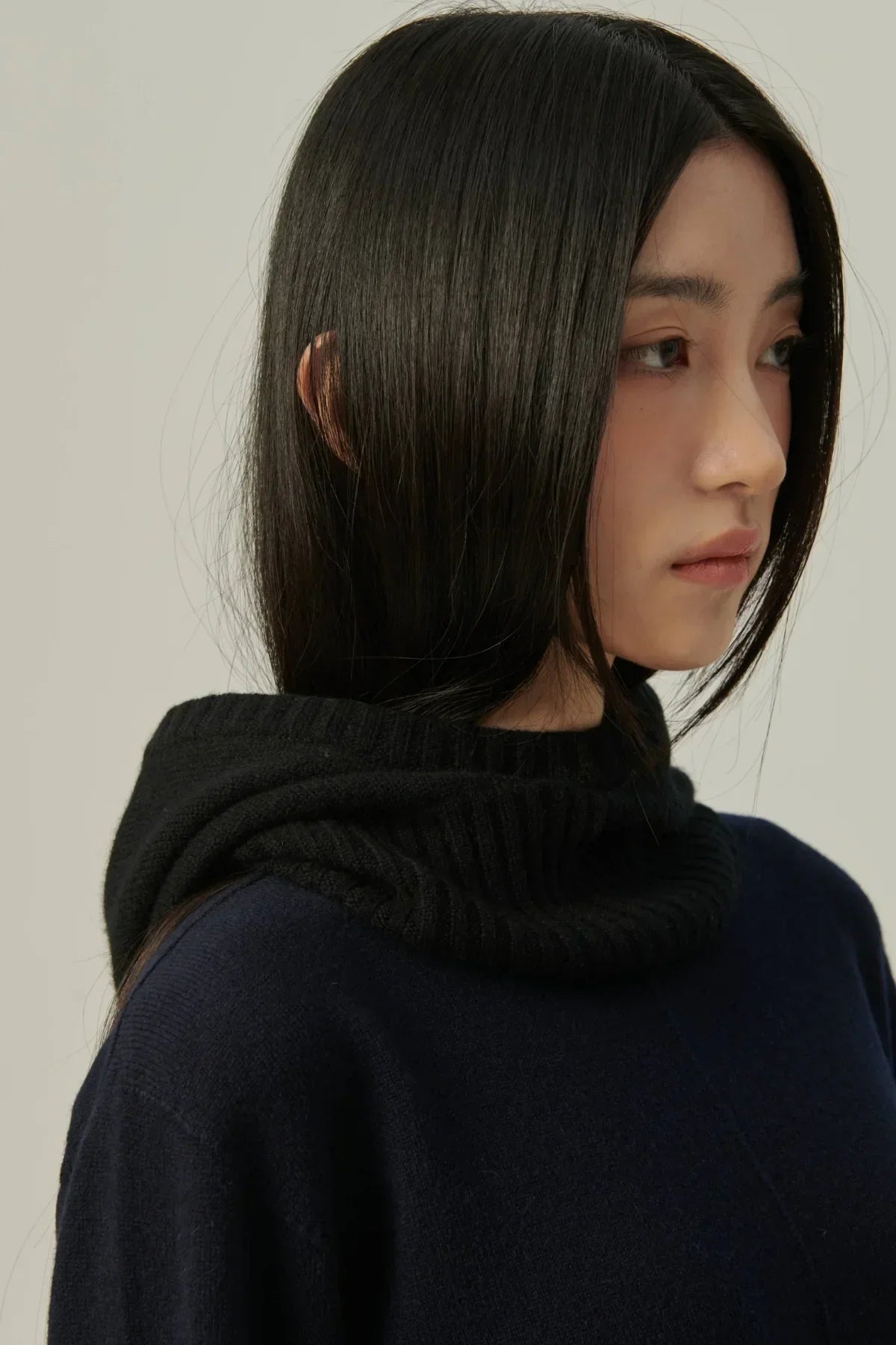 Side profile of woman wearing black cashmere balaclava and navy sweater on neutral background
