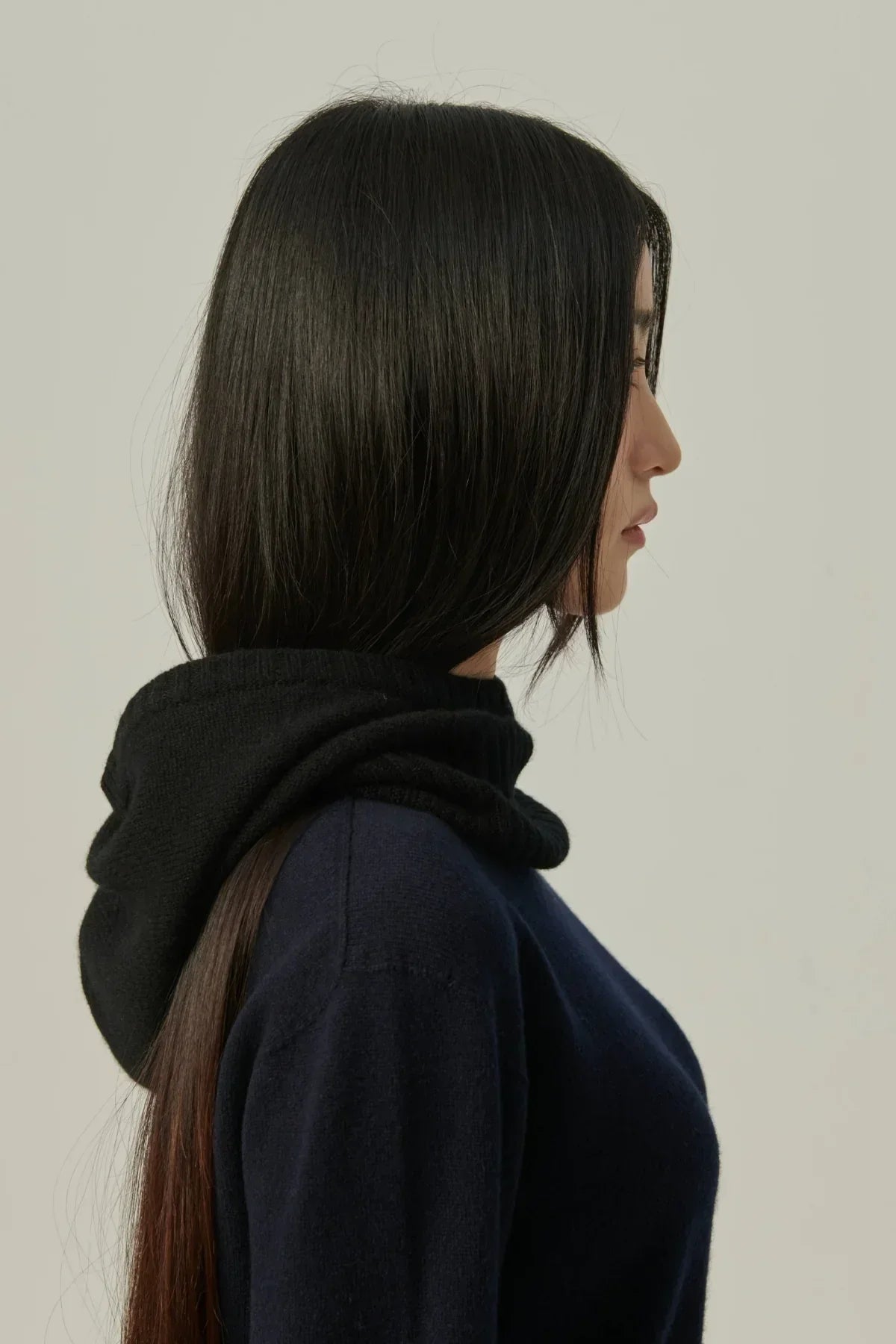 Side profile of woman with sleek black hair wearing a black cashmere balaclava hood and navy sweater