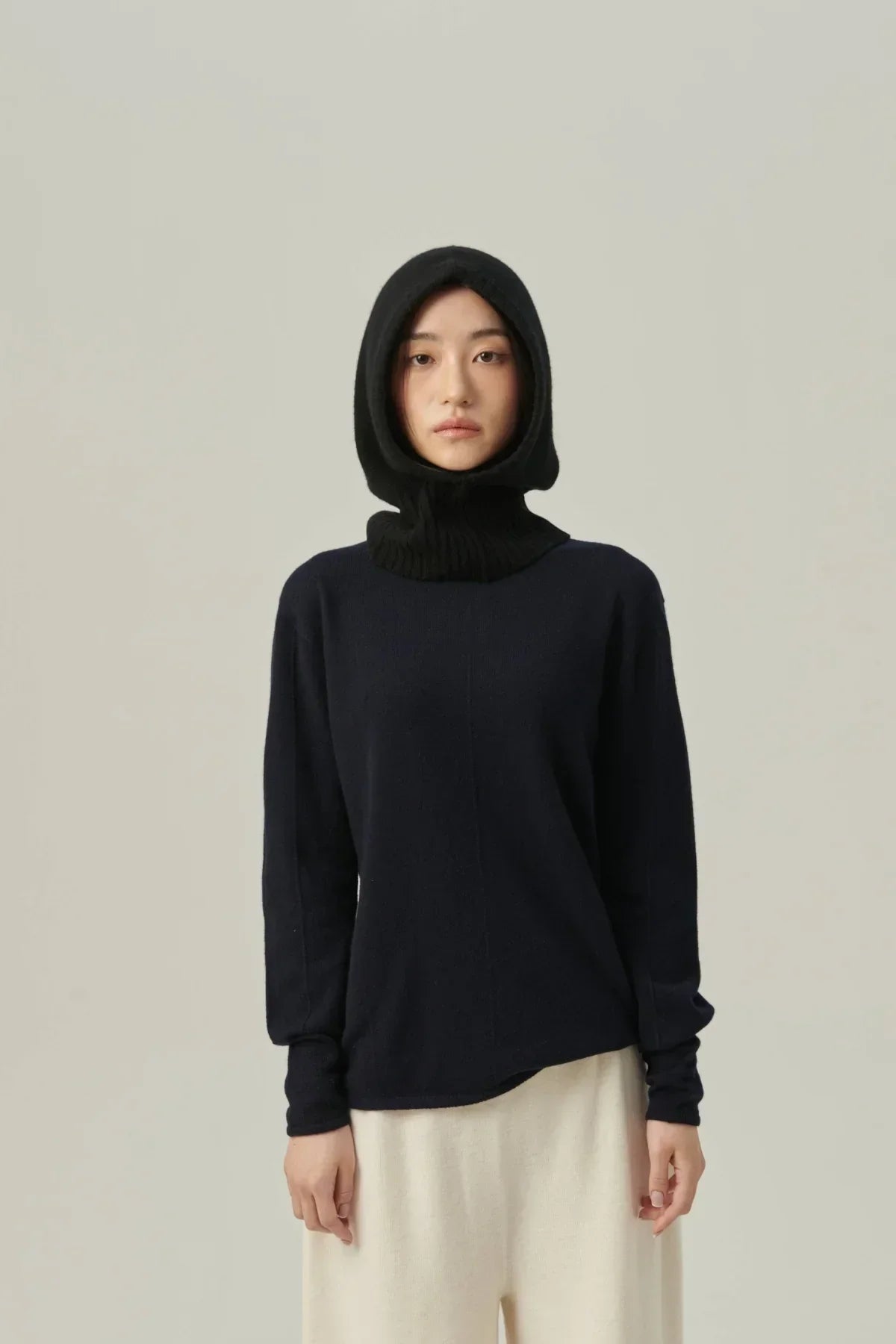 woman wearing black minimal cashmere balaclava and black sweater with cream pants on neutral background