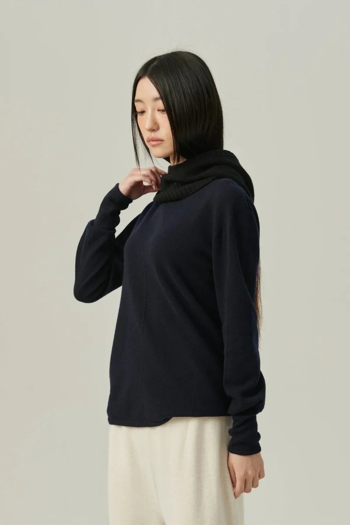 woman wearing black minimal cashmere balaclava and navy sweater with cream pants on beige background