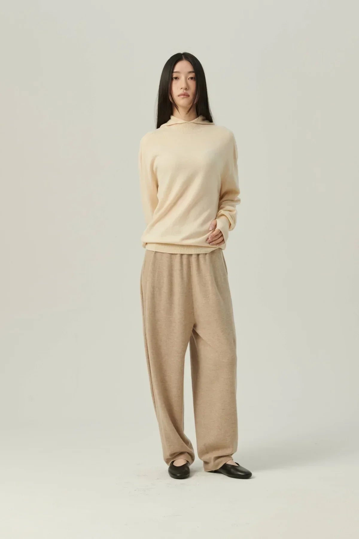 Woman wearing cream mock-neck hooded knit sweater and beige wide-leg pants with black flats
