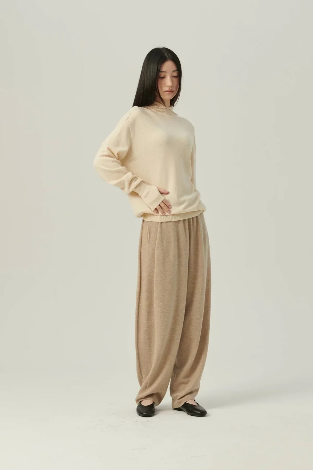 Woman wearing cream mock-neck hooded knit sweater with loose beige pants and black flats