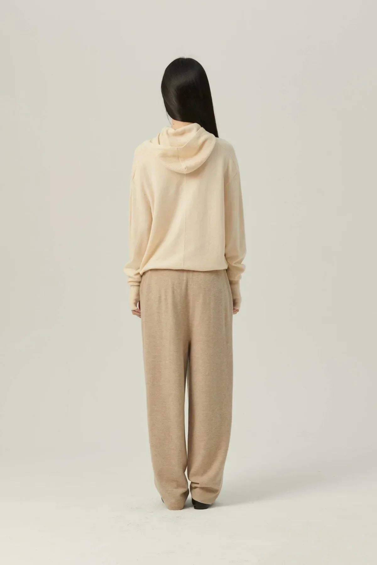 Back view of woman wearing cream mock-neck hooded knit sweater and beige wide-leg pants
