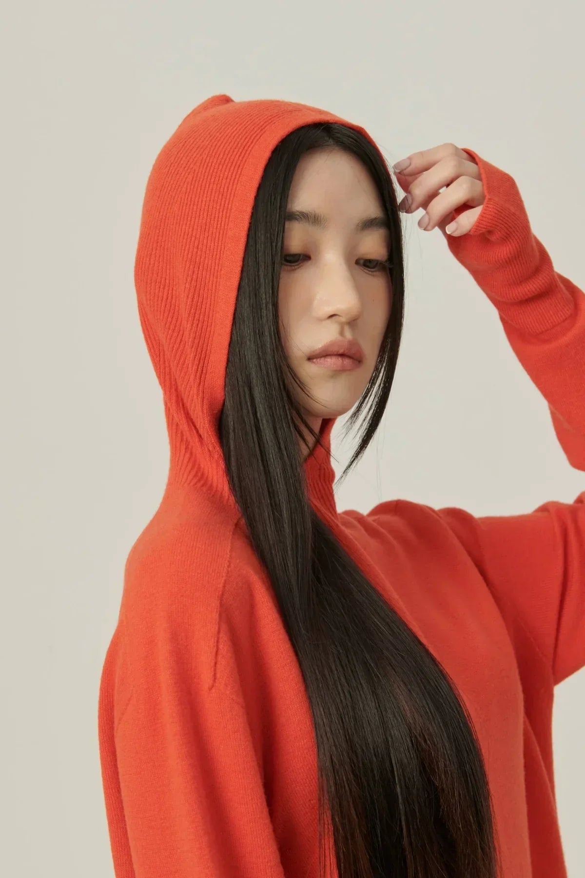 Close-up of a woman wearing an orange mock neck hooded knit sweater with long black hair