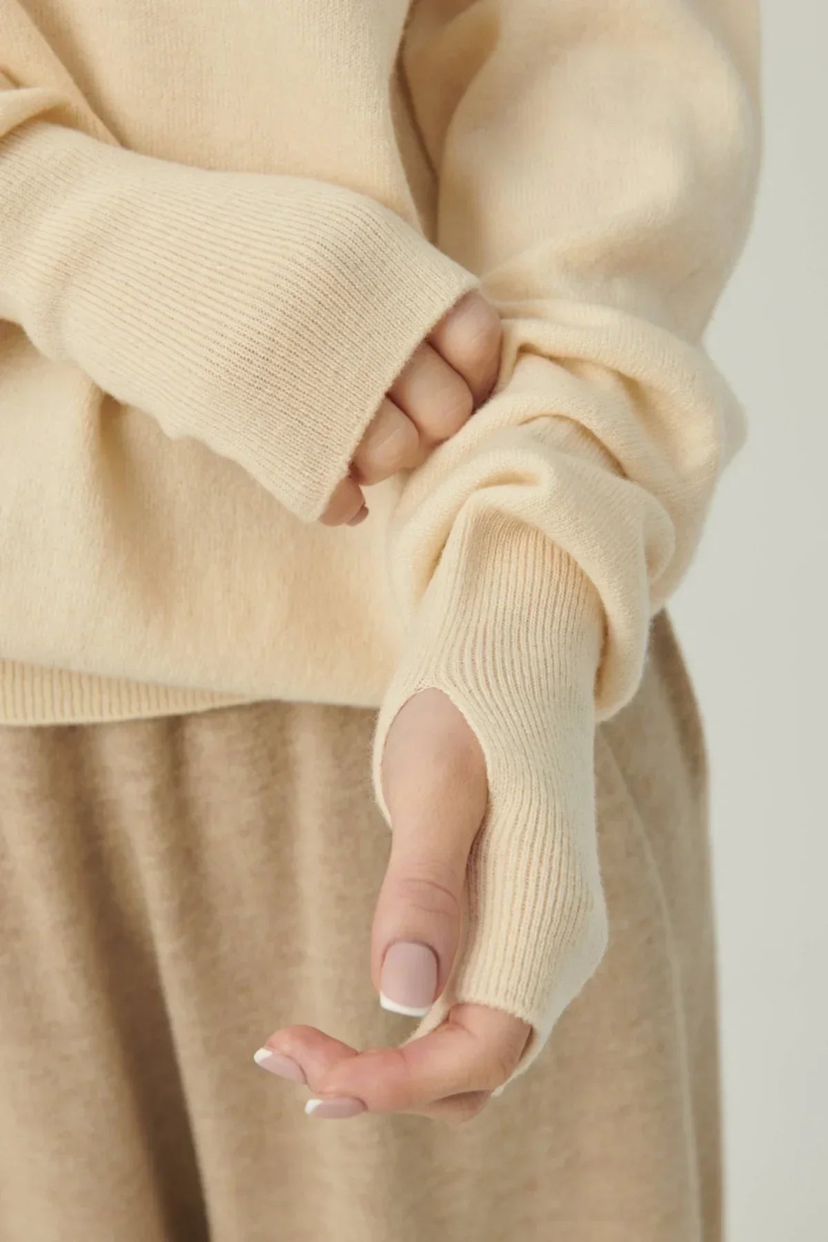 Close-up of beige knit sweater sleeve with thumb hole on a person with manicured nails