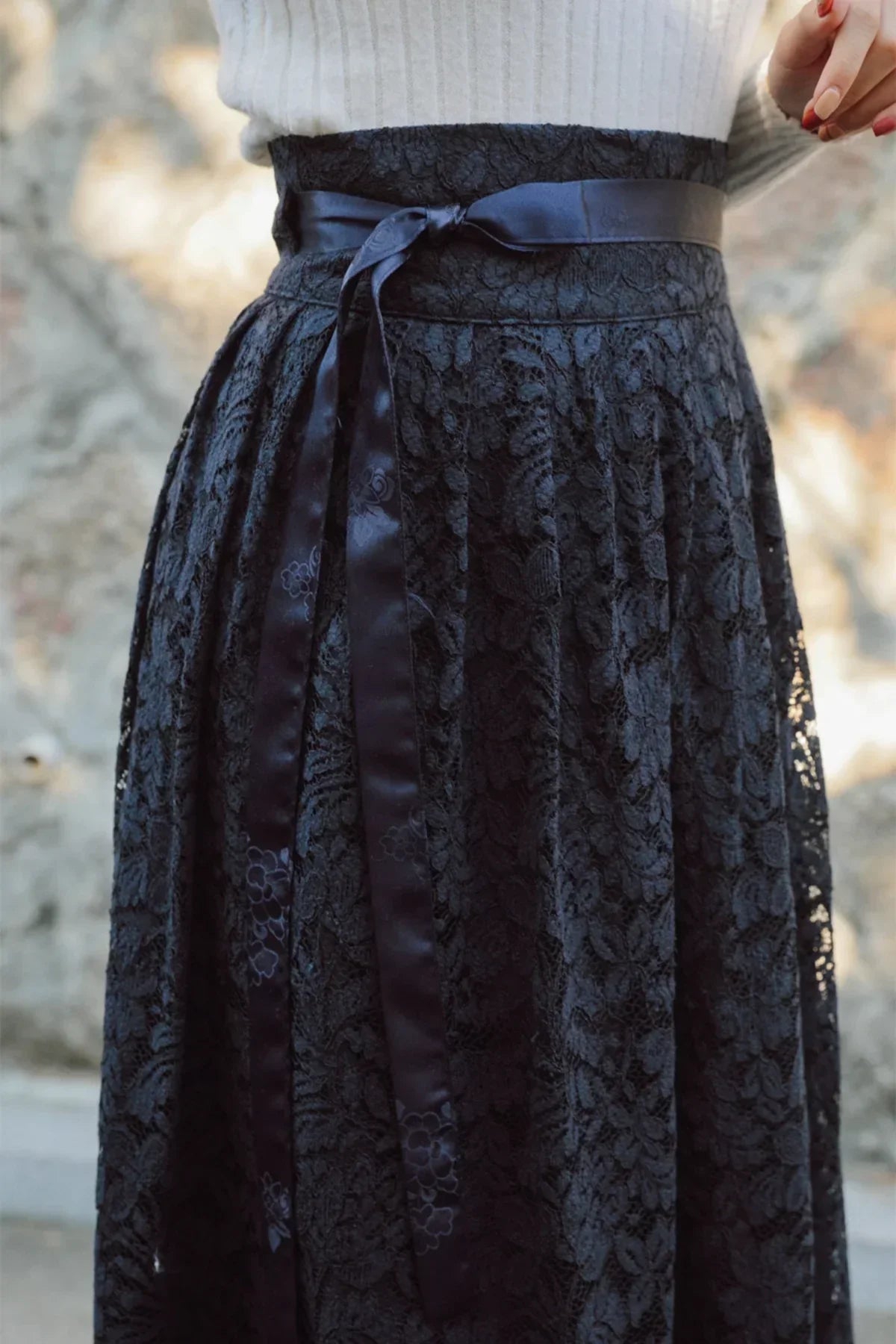 Close-up of black long lace skirt with floral pattern and satin ribbon tied at the waist