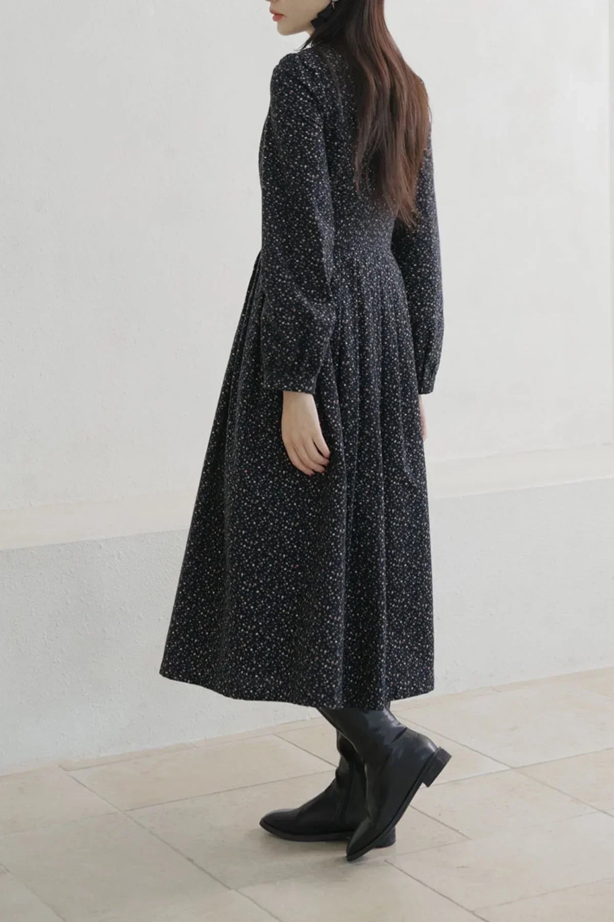 Woman wearing long black floral dress with puff sleeves and black ankle boots on tiled floor