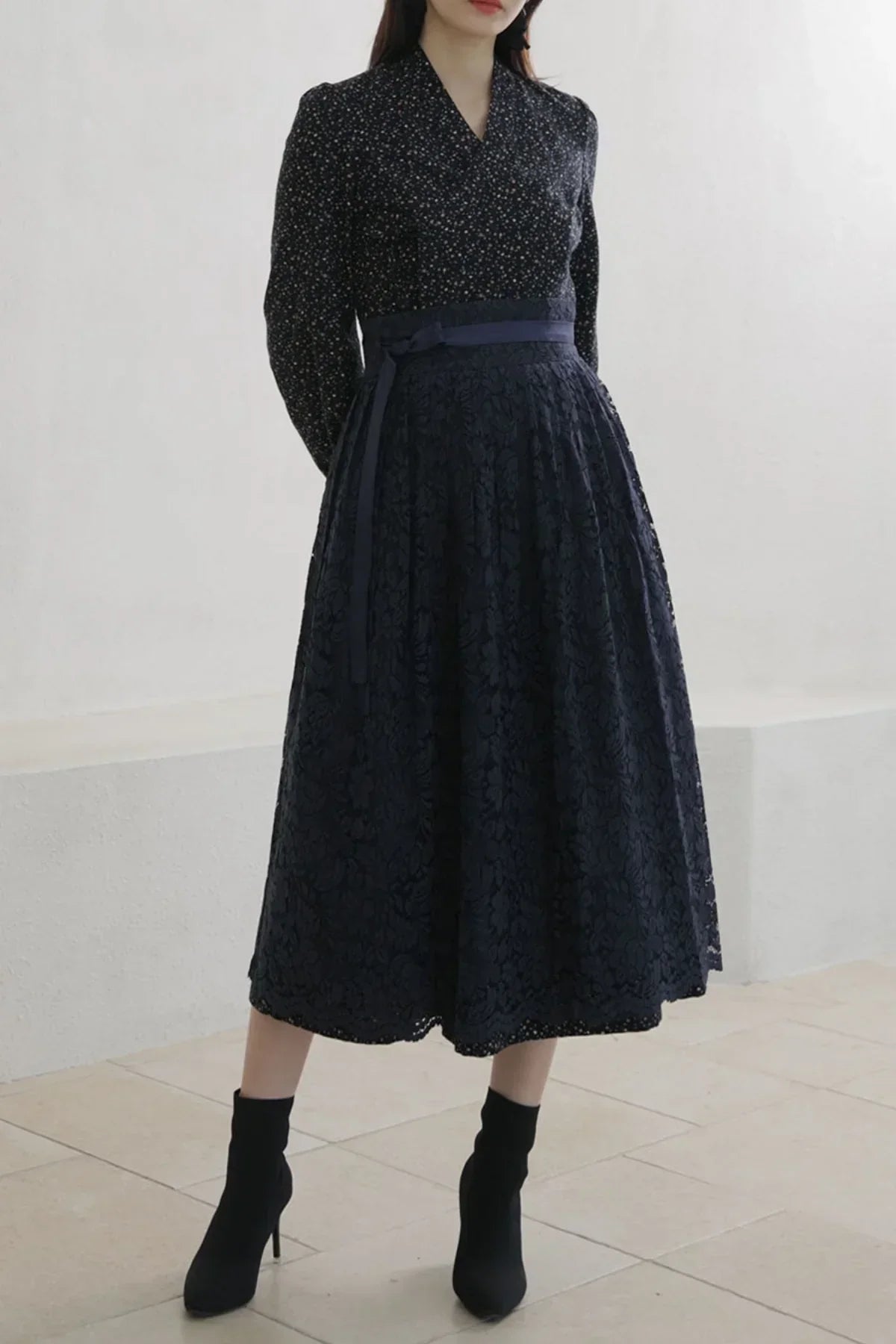 Woman wearing a black floral lace midi skirt with a tied belt and black ankle boots