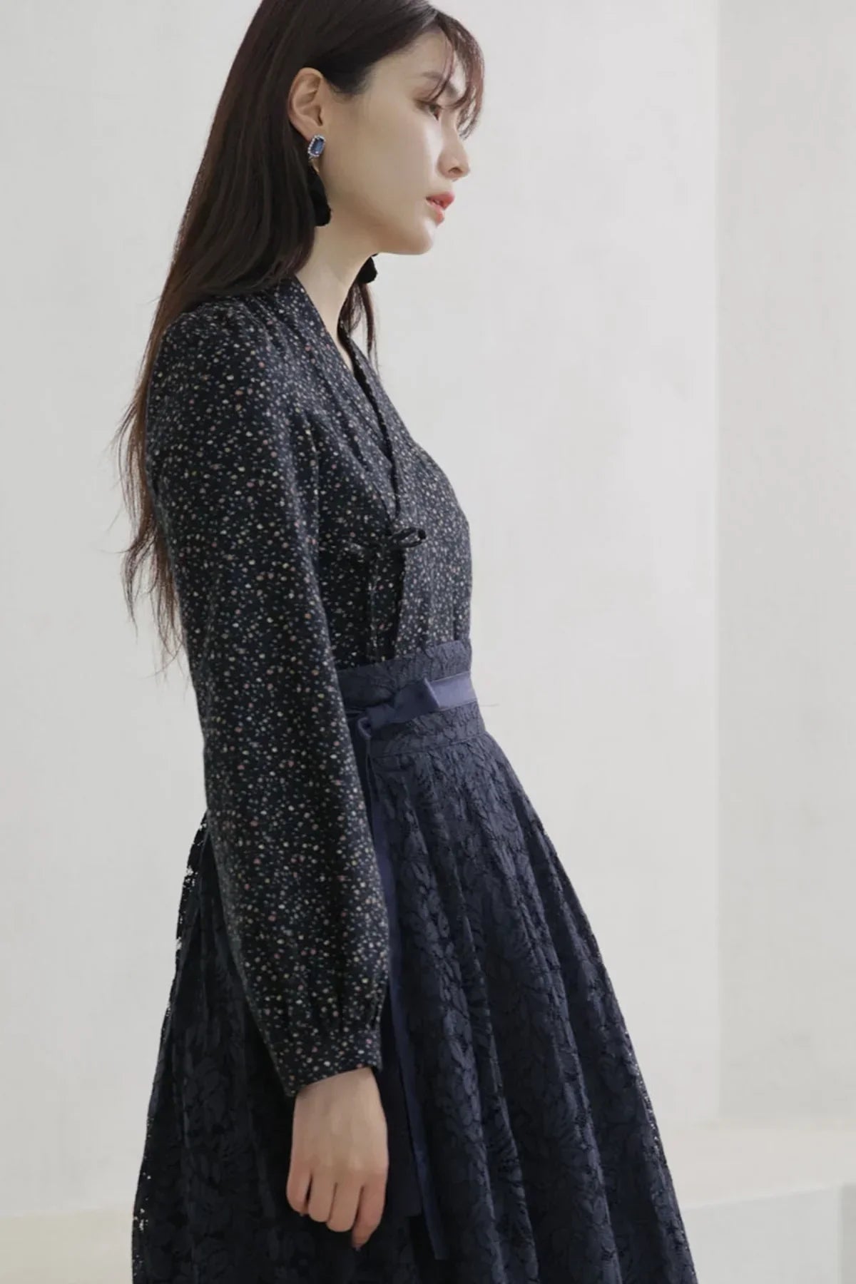 Side profile of woman wearing navy blue floral long sleeve blouse and lace skirt with bow sash