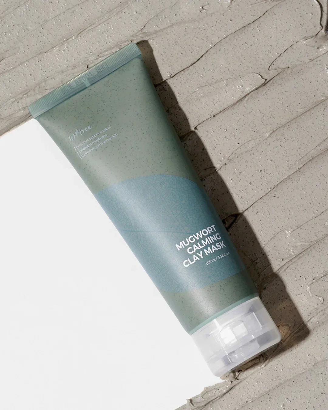 Tube of mugwort calming clay mask on textured clay surface, natural skincare product