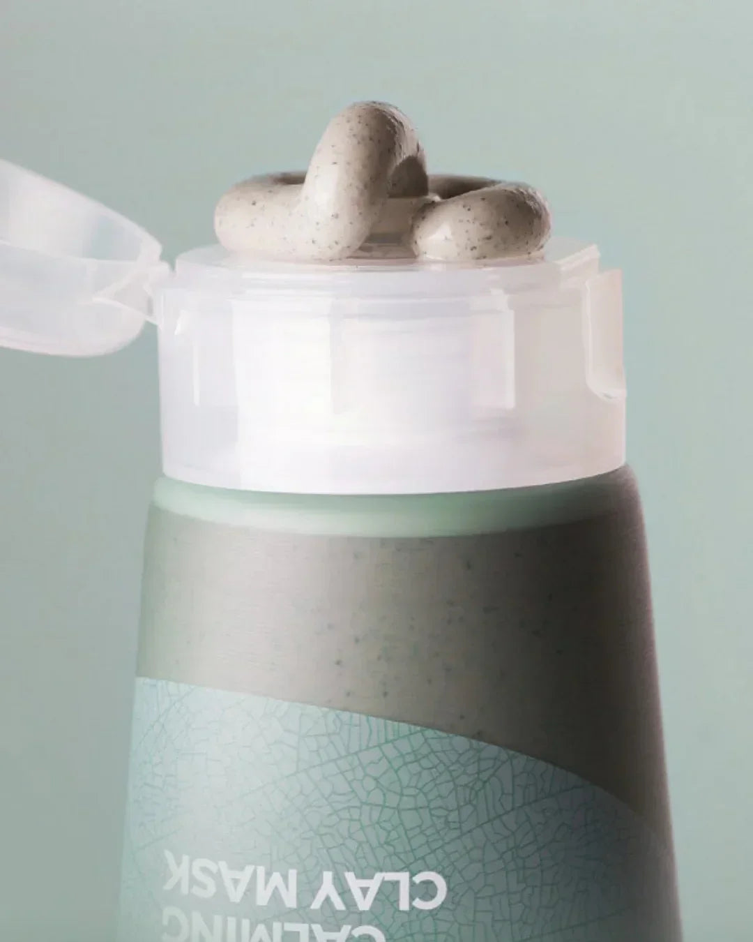 Close-up of opened tube dispensing light green mugwort calming clay mask with speckles