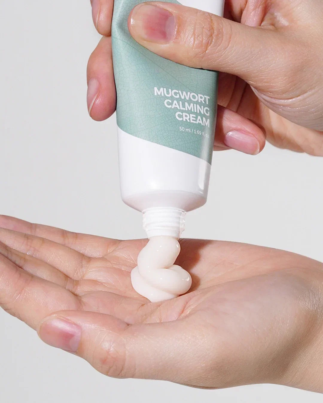 Hand squeezing mugwort calming cream from a green and white 50ml tube onto palm