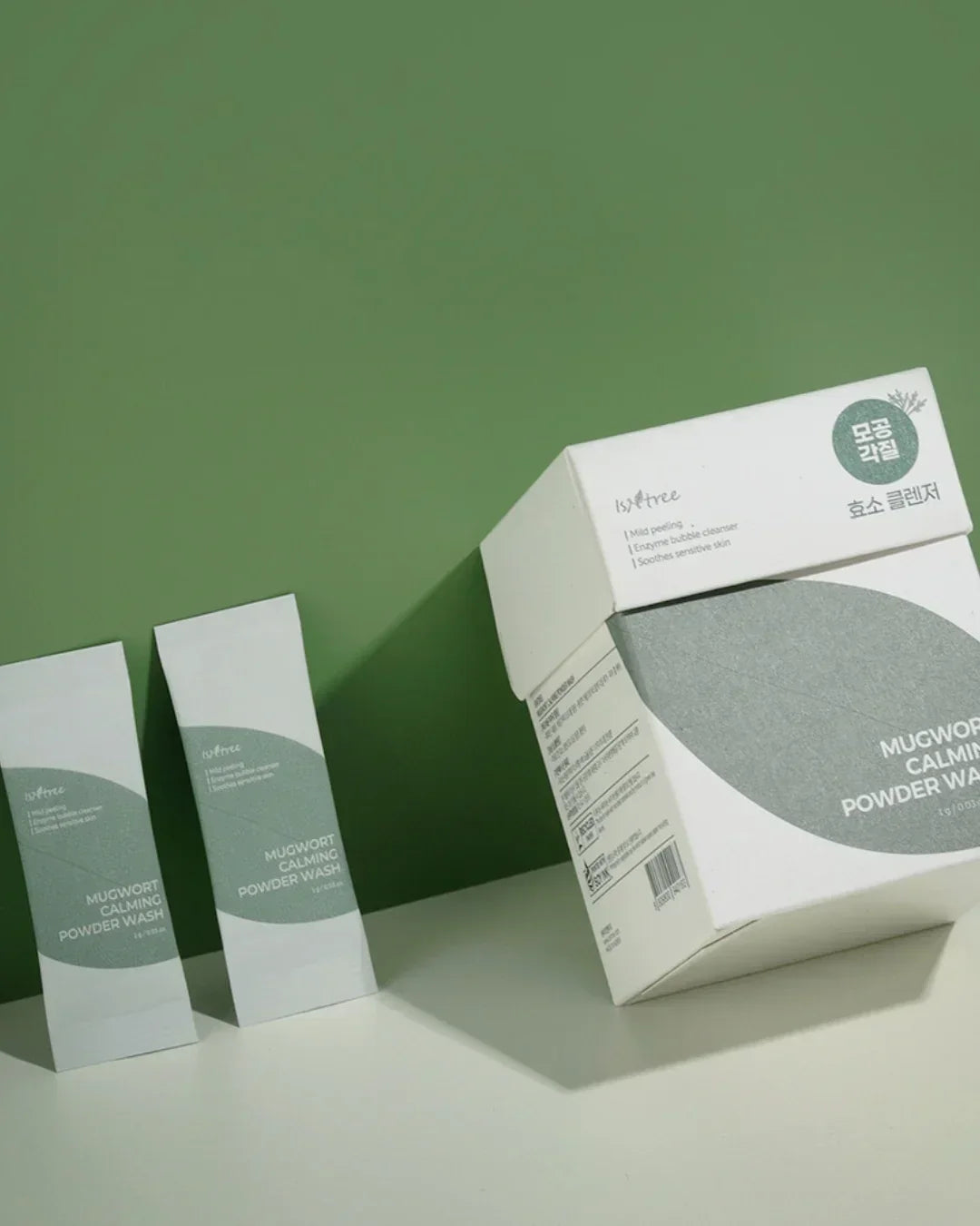 Isntree Mugwort Calming Powder Wash packaging with small sachets and a large box on green and white surface
