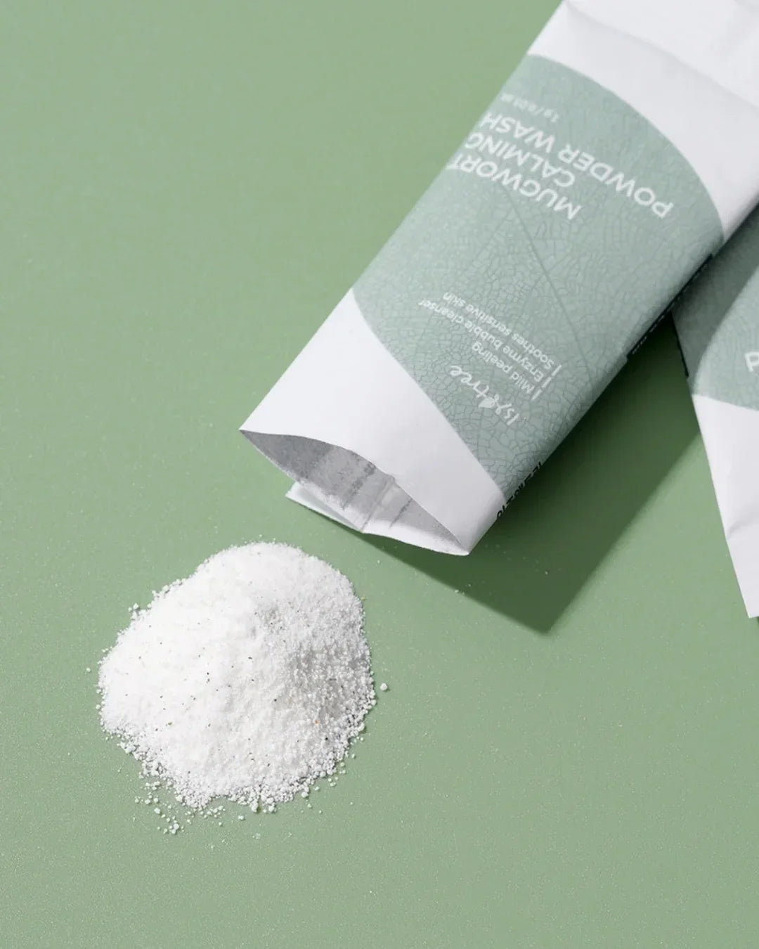 Mugwort calming powder wash sachets with spilled white powder on green surface