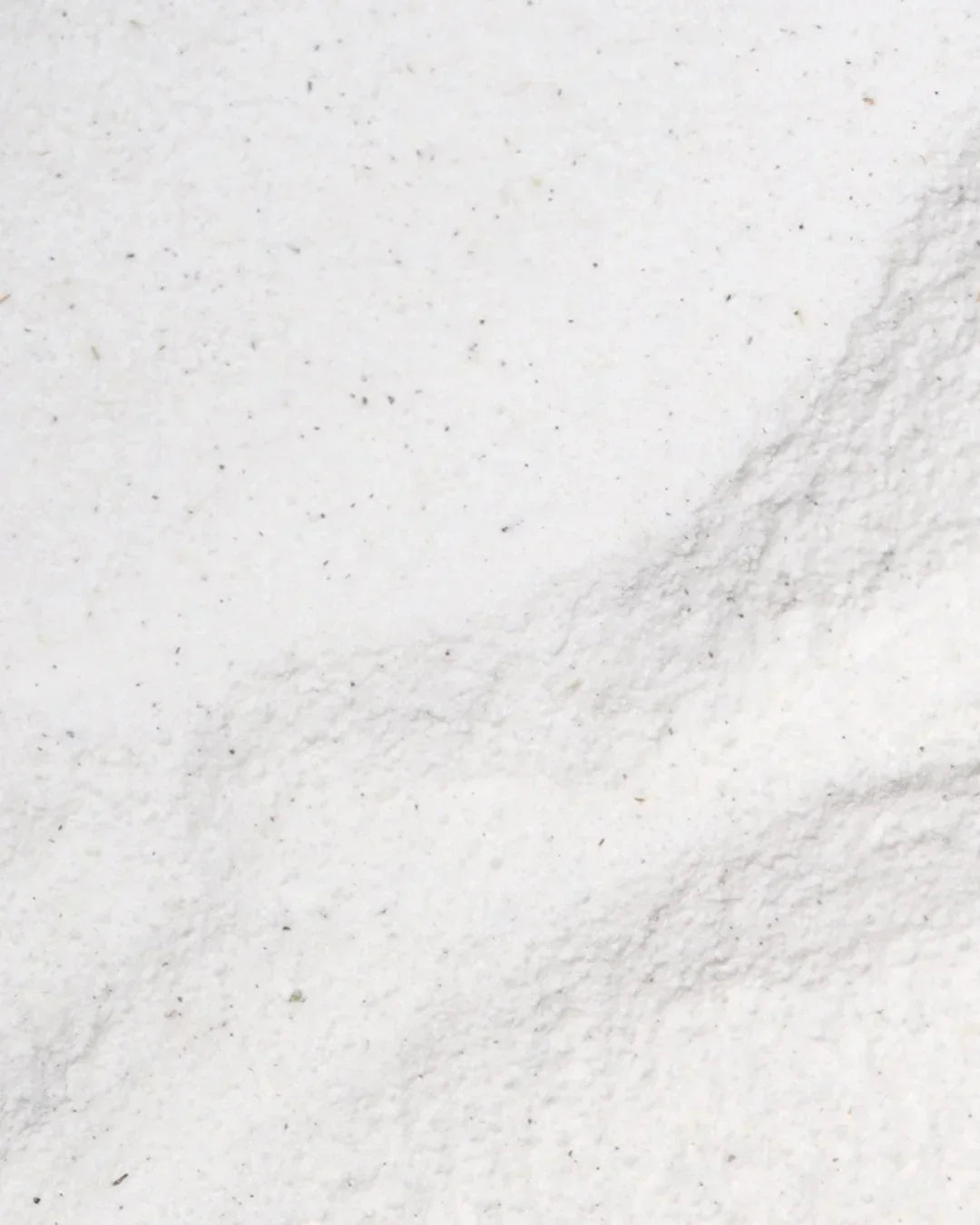 Close-up texture of fine white mugwort calming powder with small dark flecks