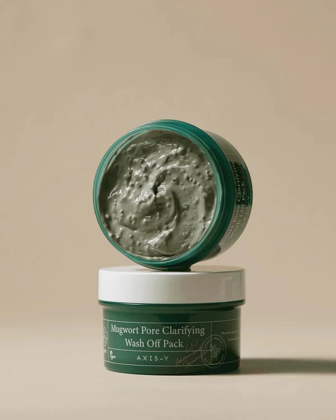 Open jar of Axis-Y Mugwort Pore Clarifying Wash Off Pack with textured green clay product on beige background