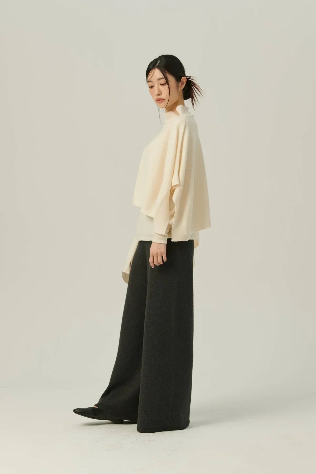 Model wearing ivory multiway knit cape, black wide-leg pants, and black shoes on neutral background
