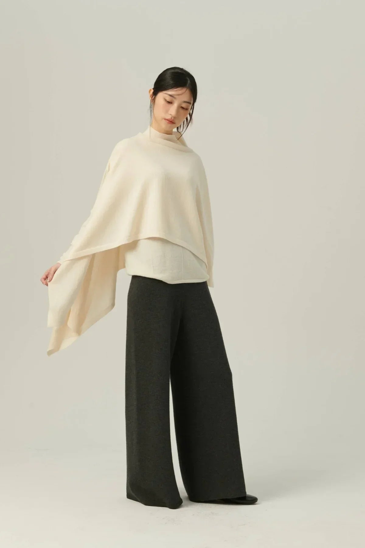 Woman wearing ivory knit multiway cape with black wide-leg pants in studio