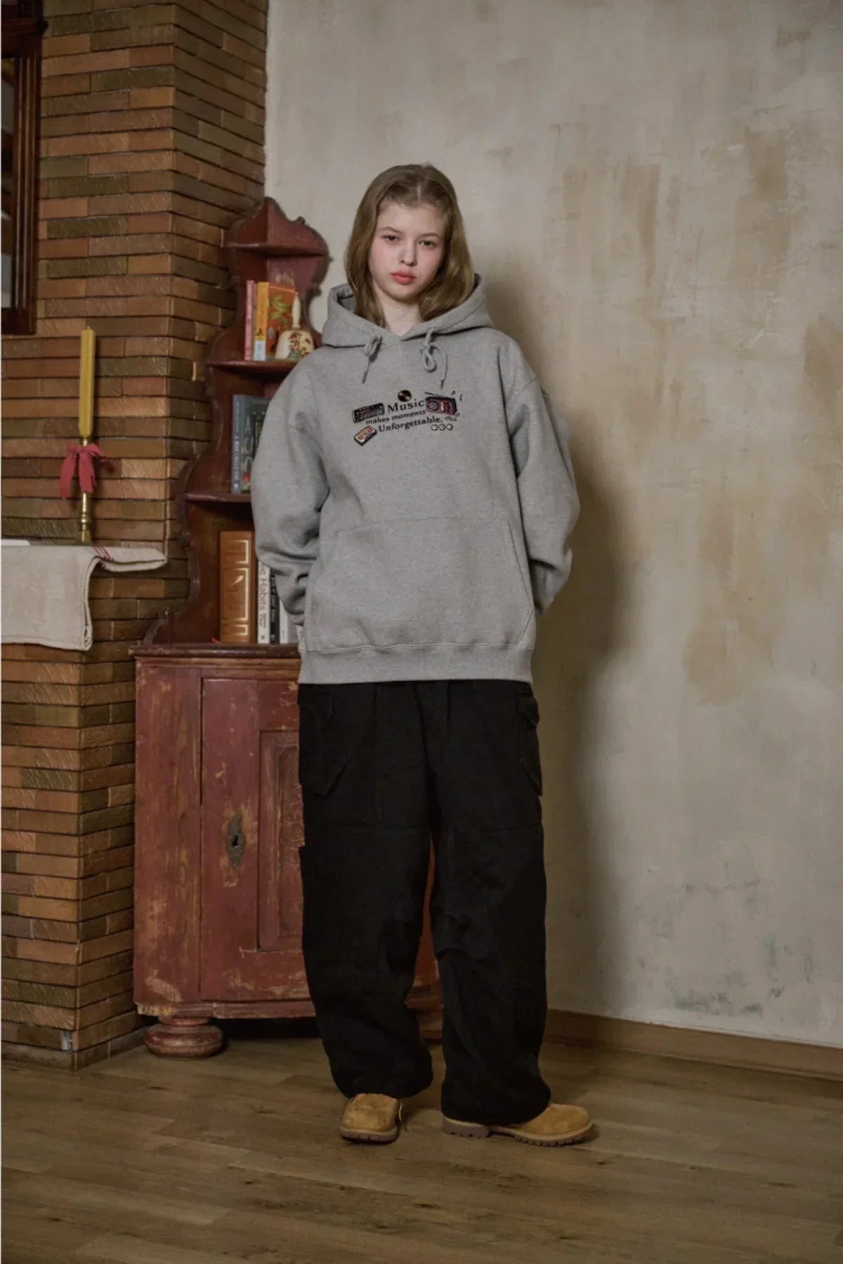 Woman wearing gray embroidered Music Moments hoodie with black wide pants and tan boots in vintage room