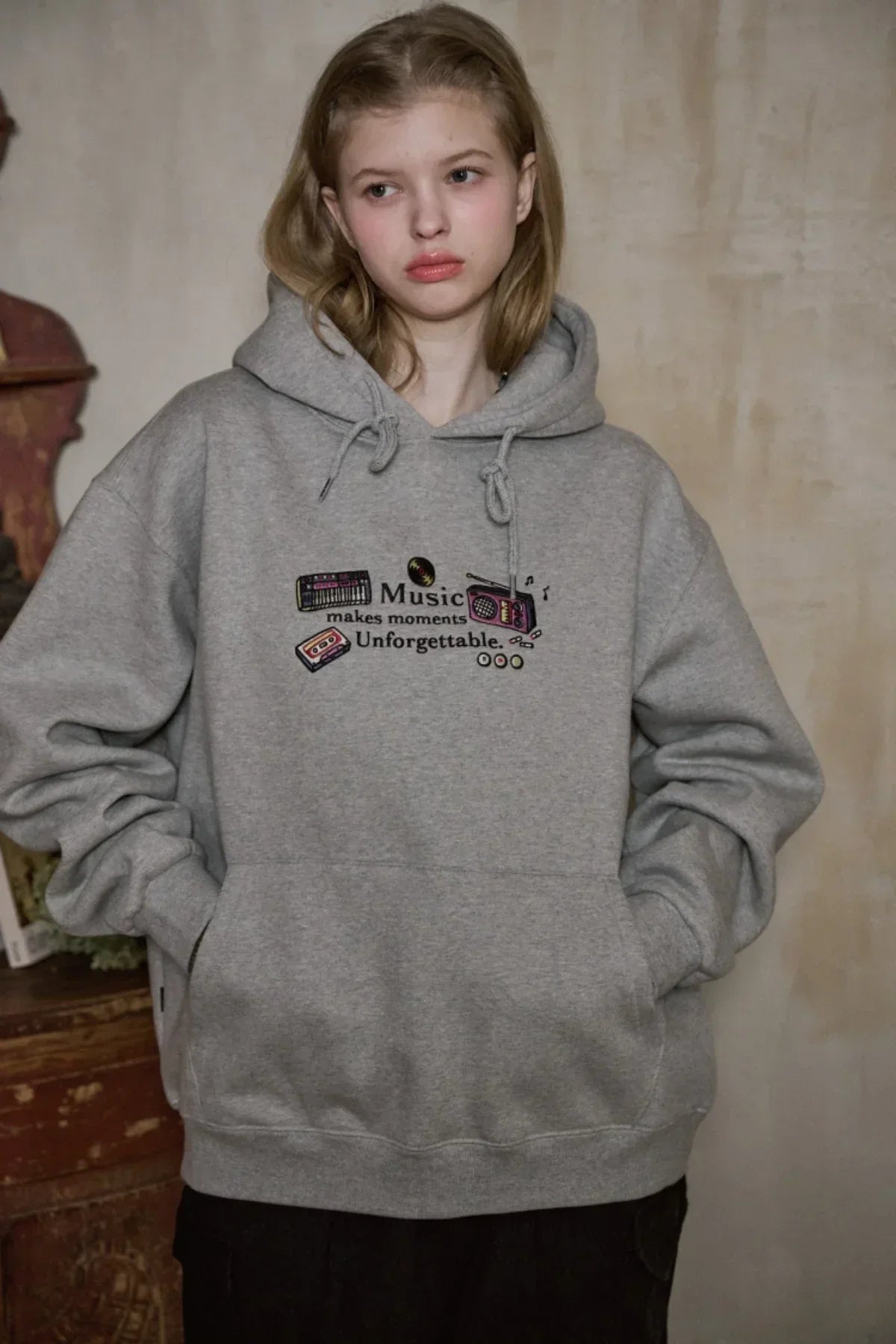 Young woman wearing a gray hoodie with embroidered vintage music designs and the phrase 'Music makes moments Unforgettable'