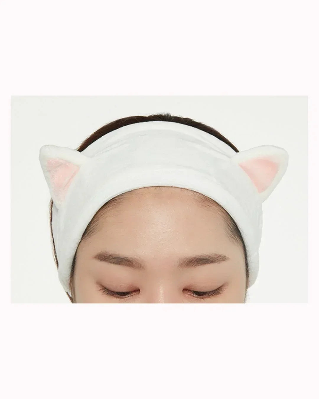 Close-up of person wearing white plush hairband with pink cat ears against white background