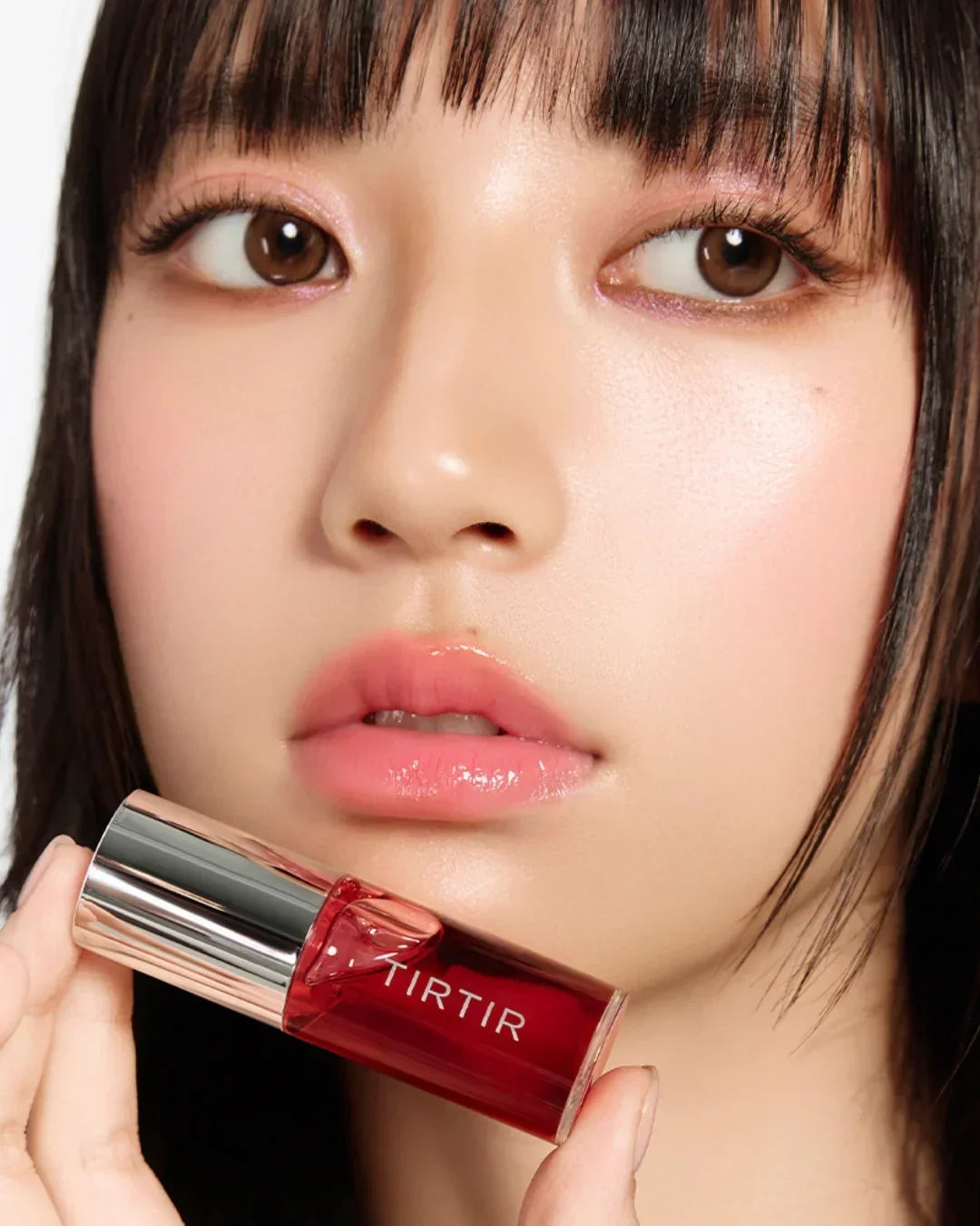 Close-up of woman with glossy pink lips holding red TIRTIR lip oil bottle