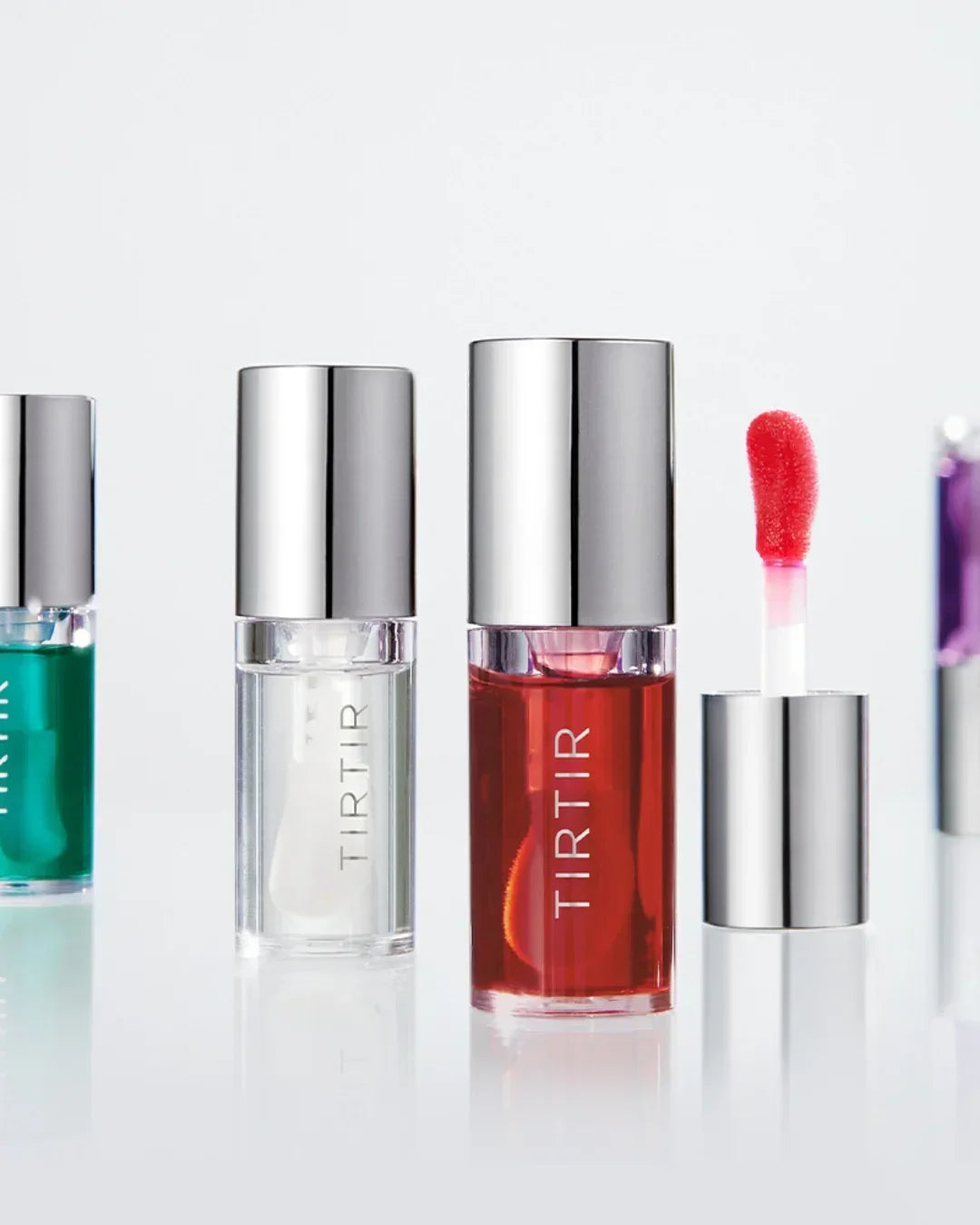 TIRTIR lip oils in clear glass bottles with silver caps, including red and clear shades on a white background