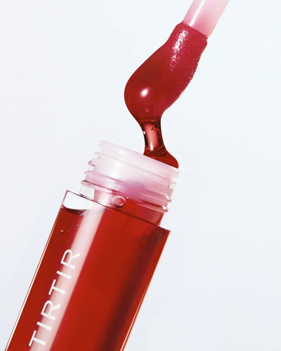 Close-up of red Tirtir glow lip oil with applicator dipped inside the bottle