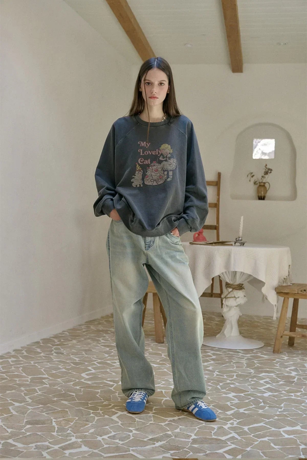 Young woman wearing dark graphic sweatshirt and baggy light jeans standing on mosaic floor indoors
