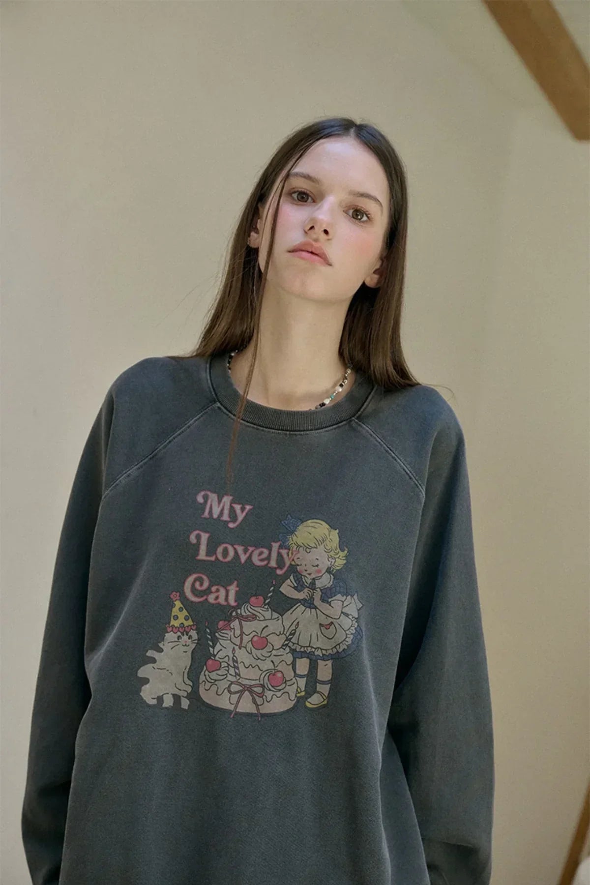 Young woman wearing smoky black sweatshirt with vintage My Lovely Cat print featuring girl and cat with cake
