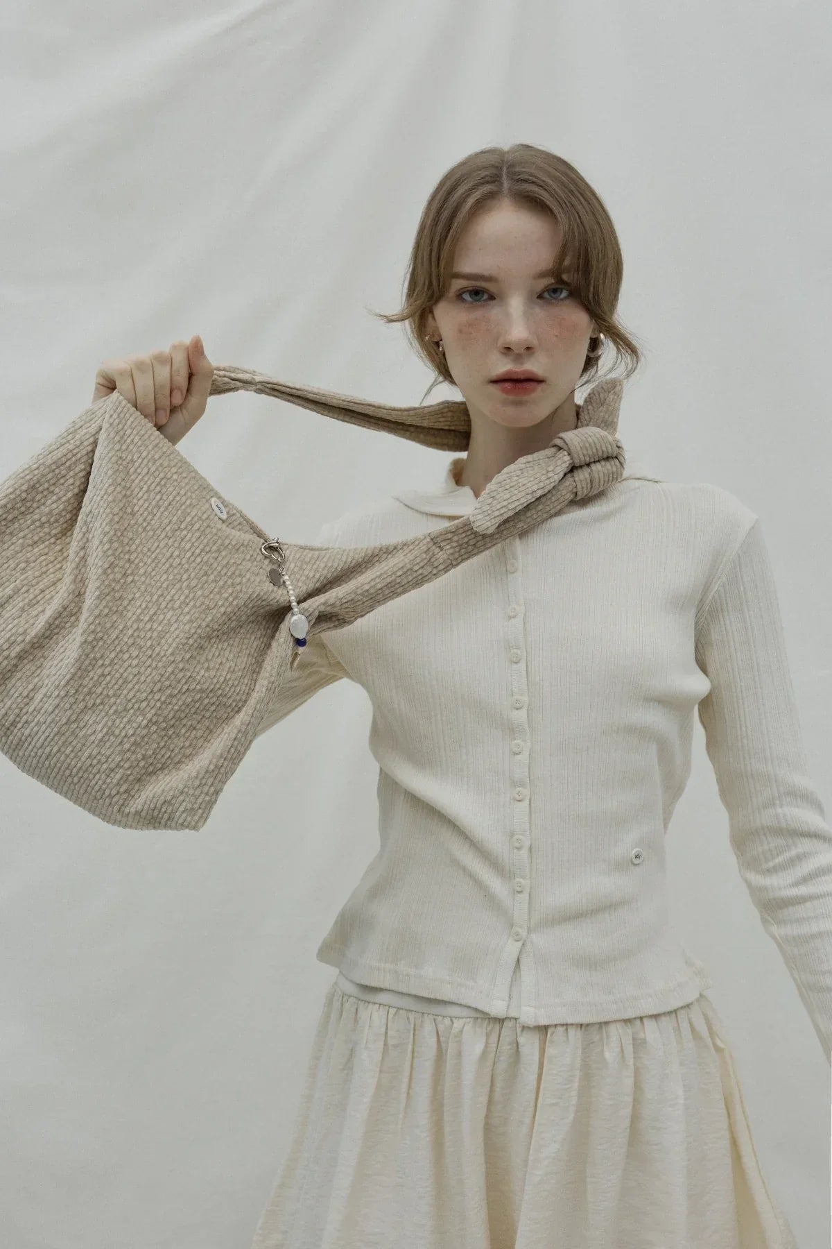 Young woman holding beige textured natural fabric knot bag against neutral background