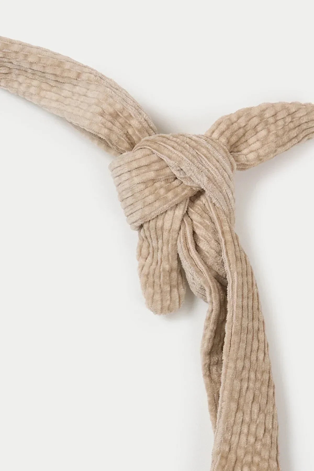 Close-up of beige natural corduroy fabric tied in a decorative knot on white background