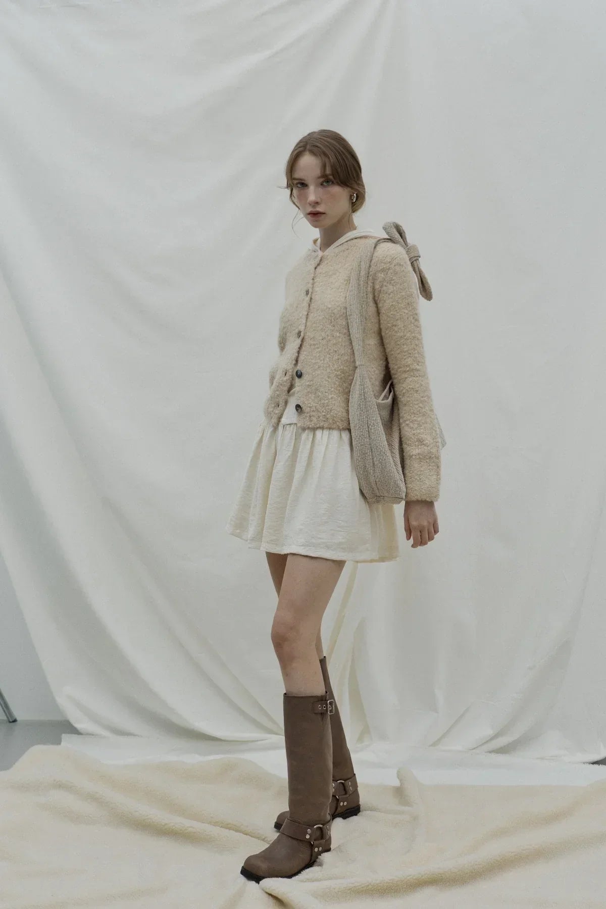 Woman in beige textured cardigan and white dress carrying knitted natural knot bag with bow detail