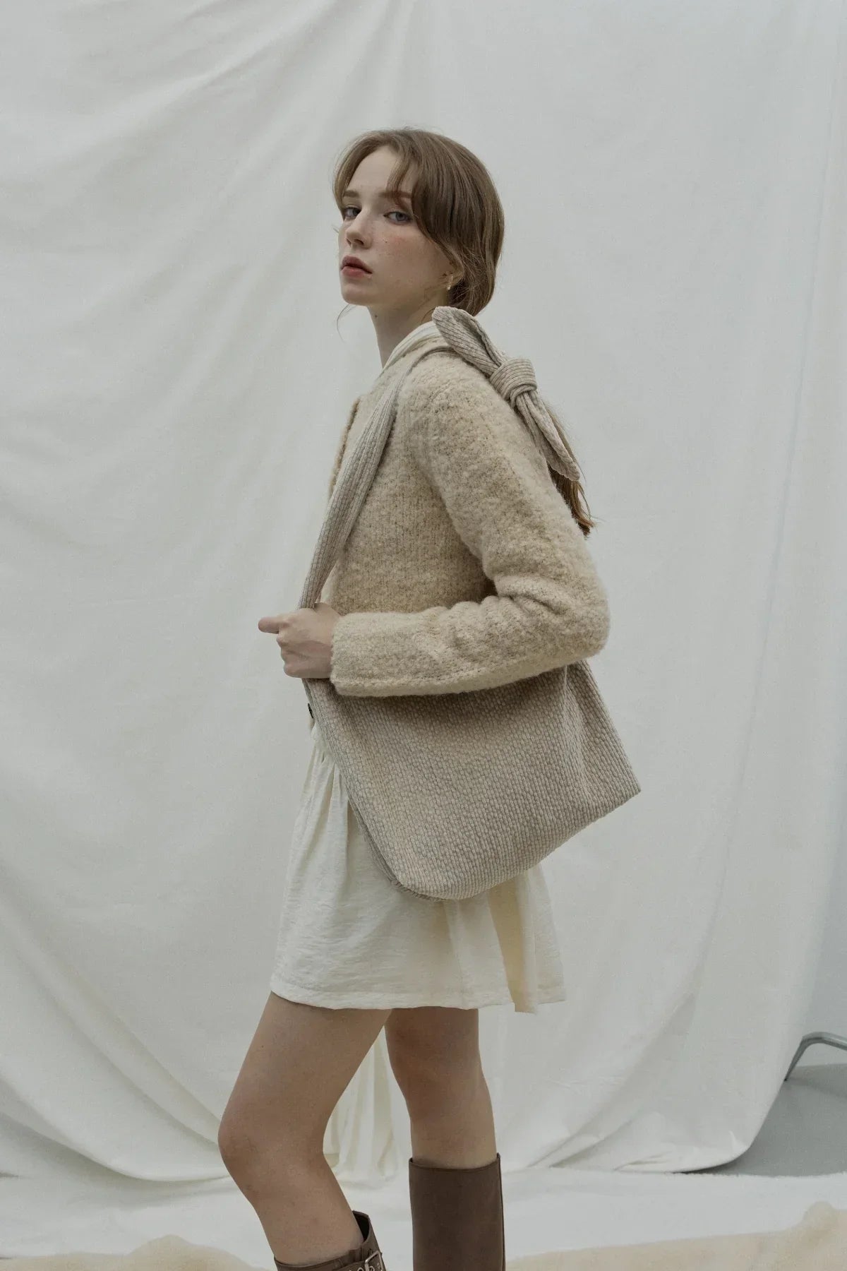 Woman wearing beige knit sweater and white dress carrying a large beige natural knot bag on shoulder