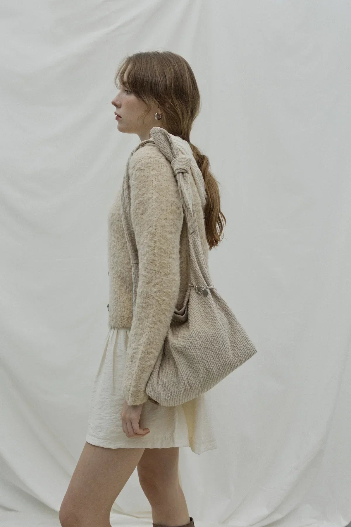 Side view of woman with beige natural knit knot shoulder bag and beige outfit against white backdrop