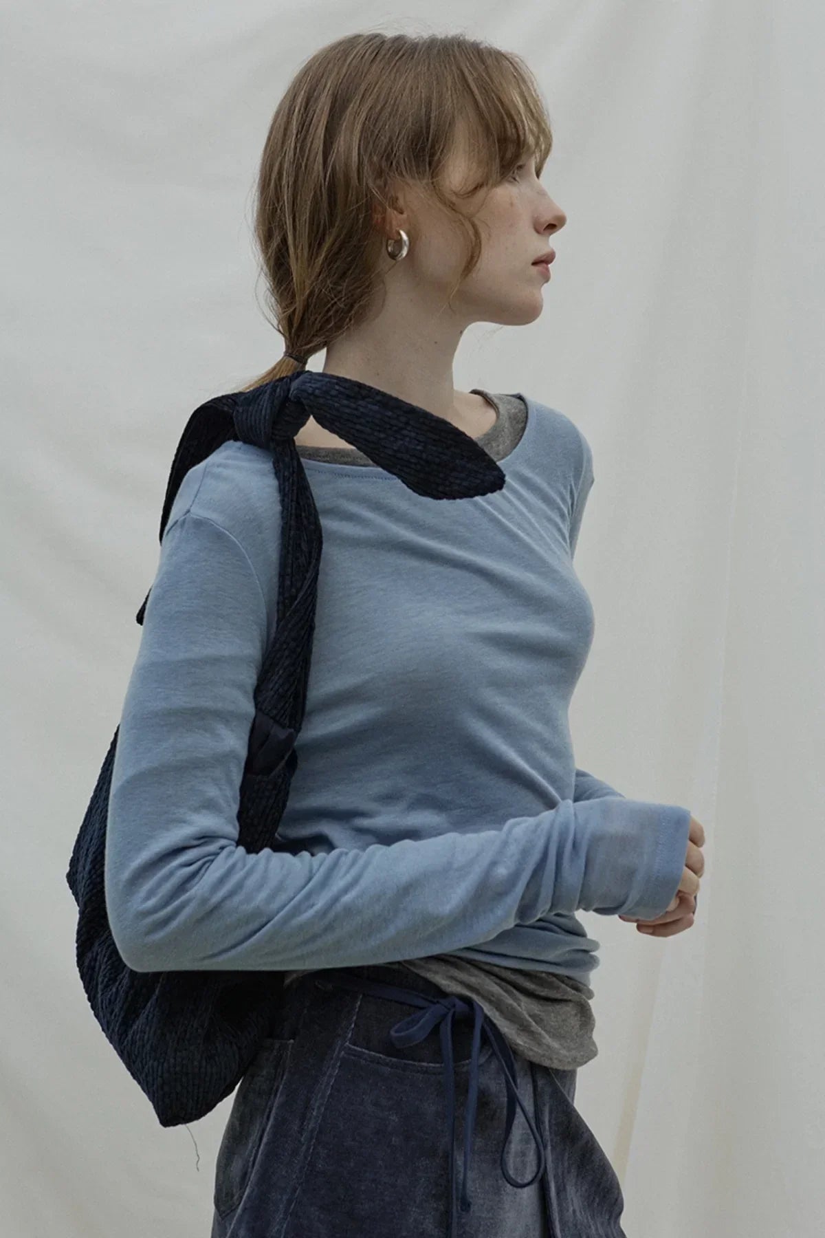 Woman wearing a light blue long-sleeve top and carrying a knotted dark navy textured bag over shoulder