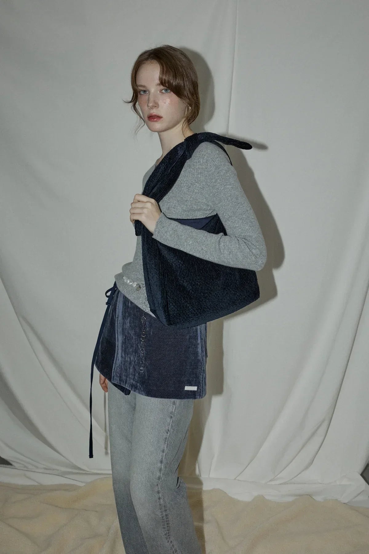 Young woman in gray sweater and denim jeans holding a dark navy natural knot bag indoors