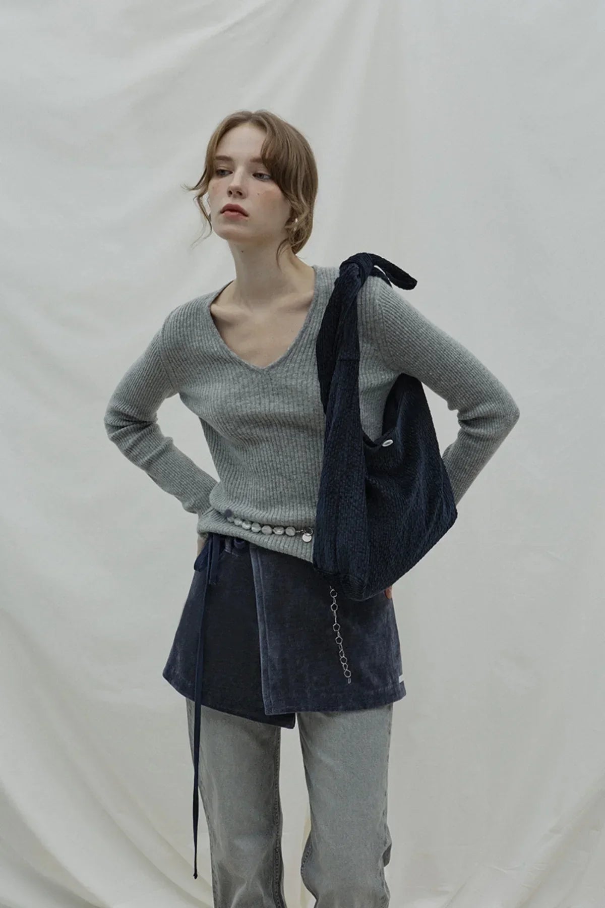 Woman wearing gray ribbed sweater and dark navy natural knot shoulder bag against plain backdrop