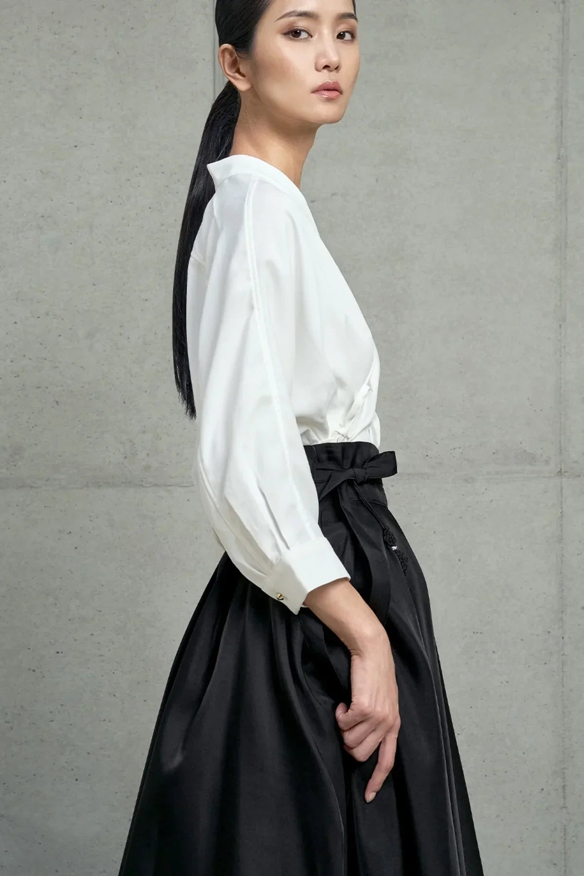 Side view of woman wearing white long sleeve blouse and black high-waisted skirt with bow detail