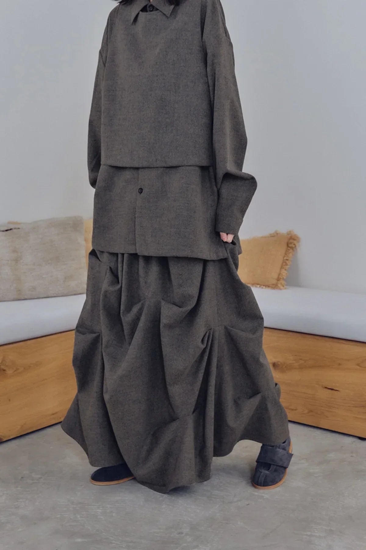 Woman wearing dark brown layered long skirt and matching shirt with black shoes in minimal room