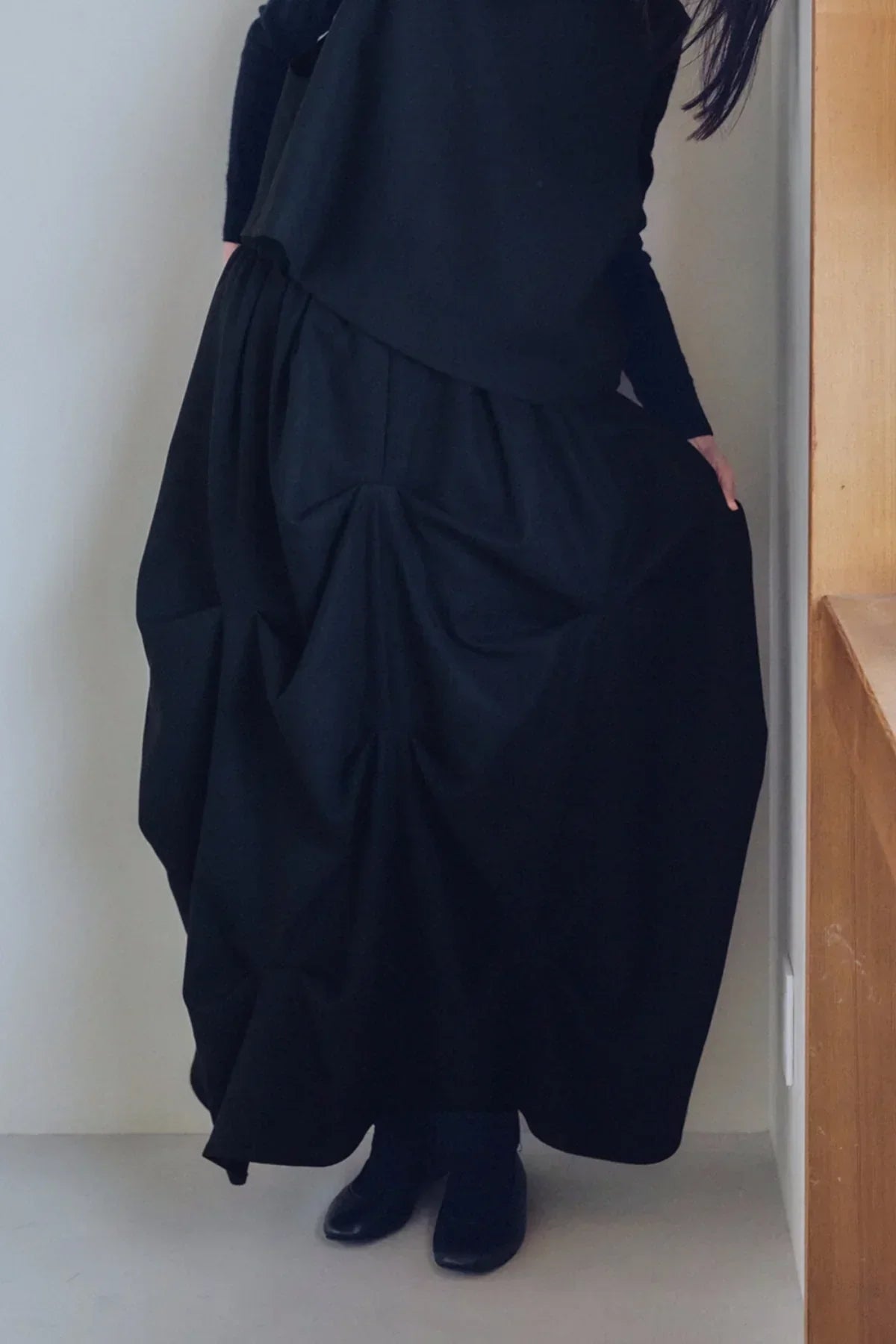 Close-up of a person wearing a black gathered skirt with a black top and black shoes indoors