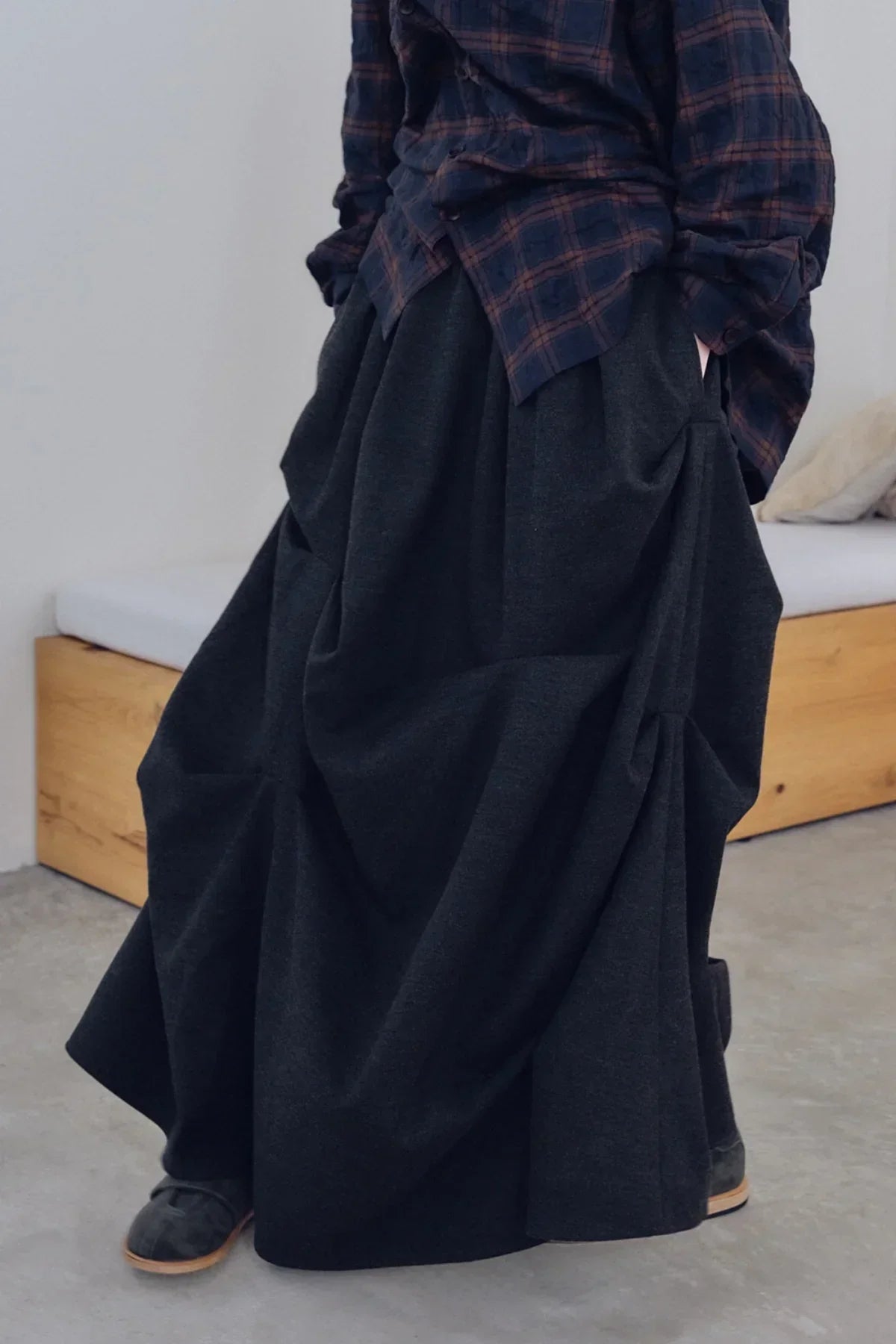 Close-up of charcoal black skirt with gathered details worn with plaid shirt and black shoes indoors