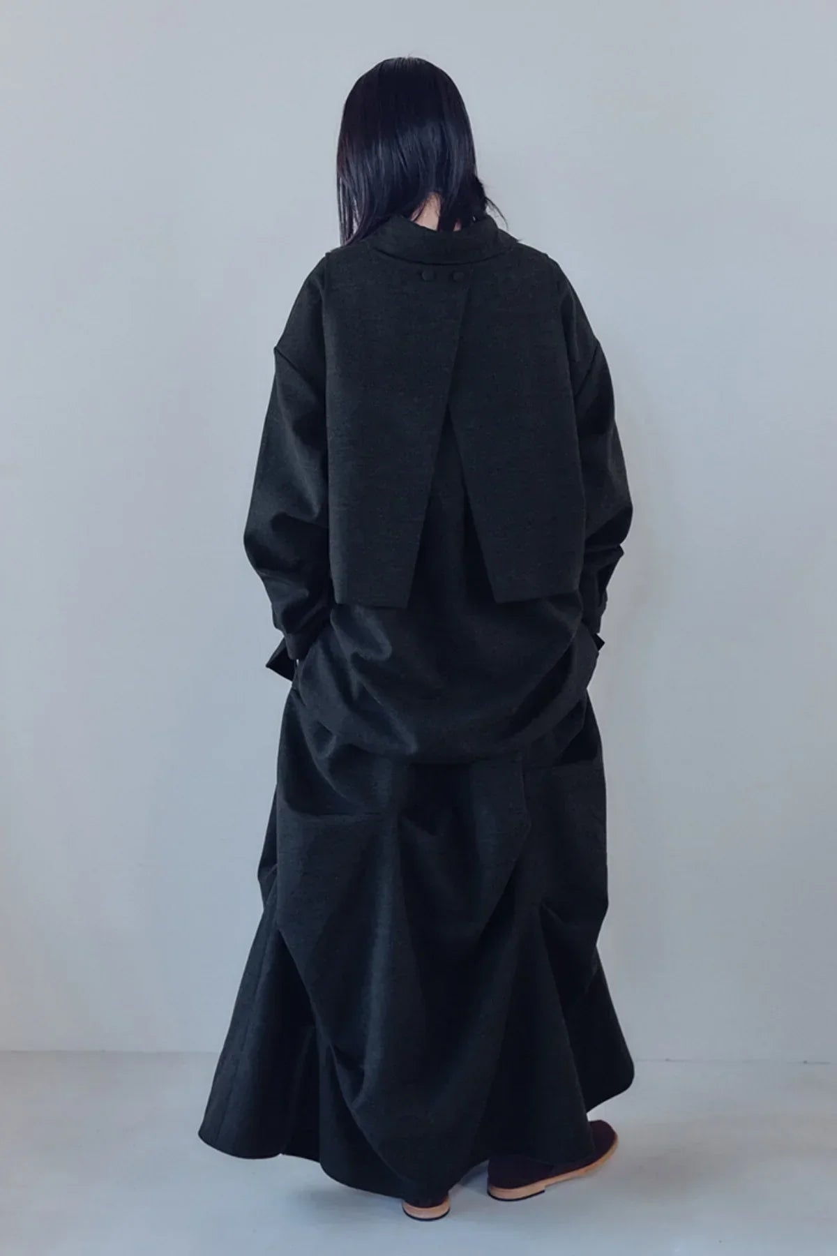 Back view of model wearing a loose charcoal black layered skirt and oversized jacket outfit